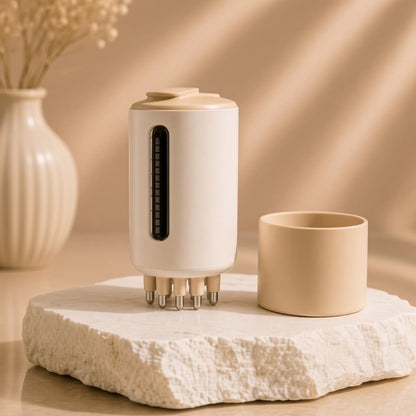 Masajeador capilar eléctrico blanco con aplicador de sérum sobre piedra decorativa, Costelya